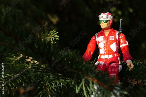 Canvas Print GI JOE action figure of military medic and rescue team member Lifeline, version from 1986, sitting on a branch of spruce tree, sunlit by bright autumn sunshine, looking like christmas tree decoration