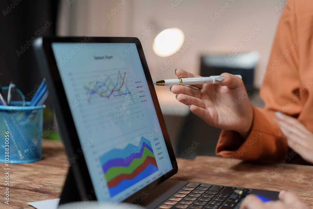 Businesswoman is pointing at a tablet computer screen displaying financial charts and graphs