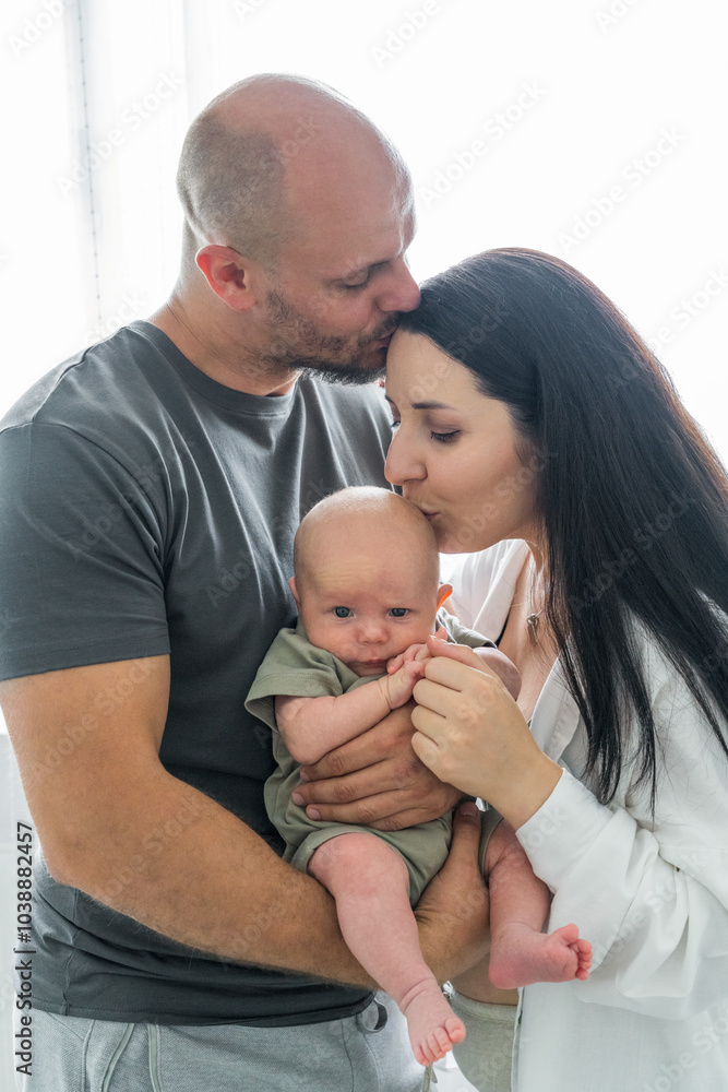 Happy parents holding newborn baby in arms. Looking at other while kissing each tenderly. Baby sleeping sweetly in cozy arms daddy. Parenthood. Happy family. Happy parents holding newborn baby in arms. Looking at other while kissing each tenderly. Baby sleeping sweetly in cozy arms daddy. Parenthood. Happy family.