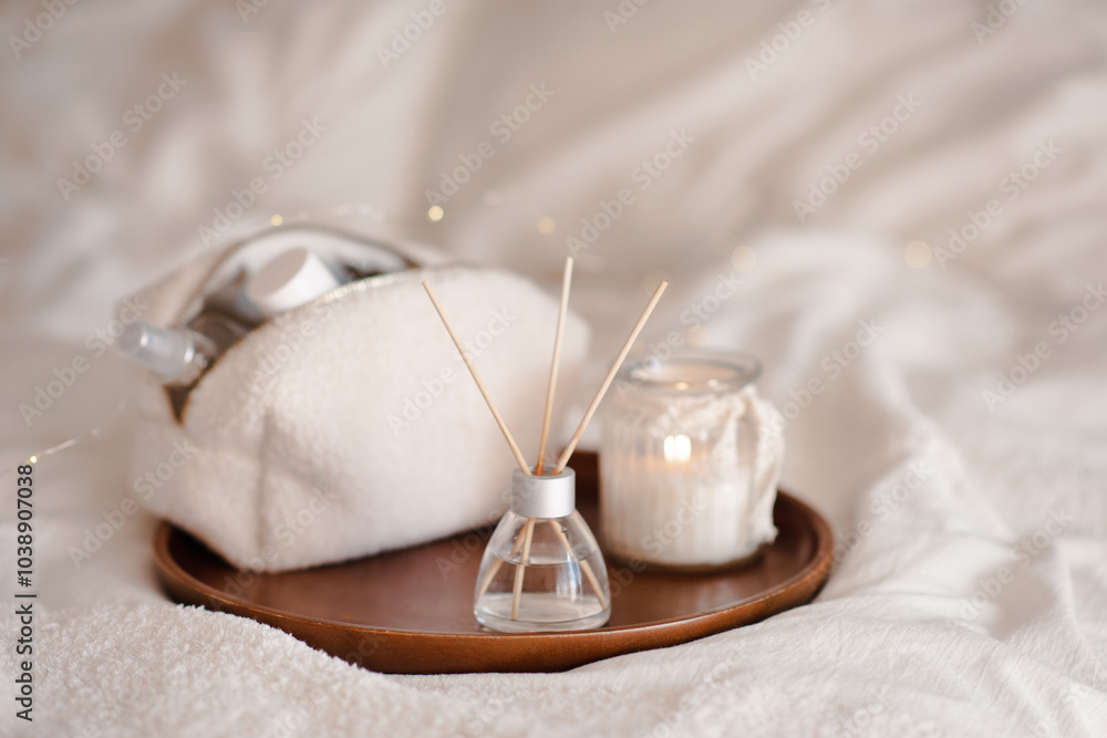 Liquid home fragrance in glass bottle with bamboo sticks with scented candle on tray in bed over white close up. Cozy atmosphere. Aromatherapy. Liquid home fragrance in glass bottle with bamboo sticks with scented candle on tray in bed over white close up. Cozy atmosphere. Aromatherapy.