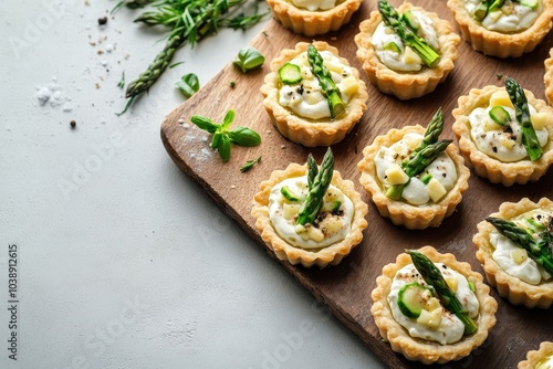 Top view of mini tarts filled with cream cheese and green asparagus on a wooden board over a light concrete surface