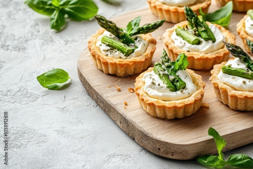 Top view of mini tarts filled with cream cheese and green asparagus on a wooden board against a light concrete backdrop Selective focus