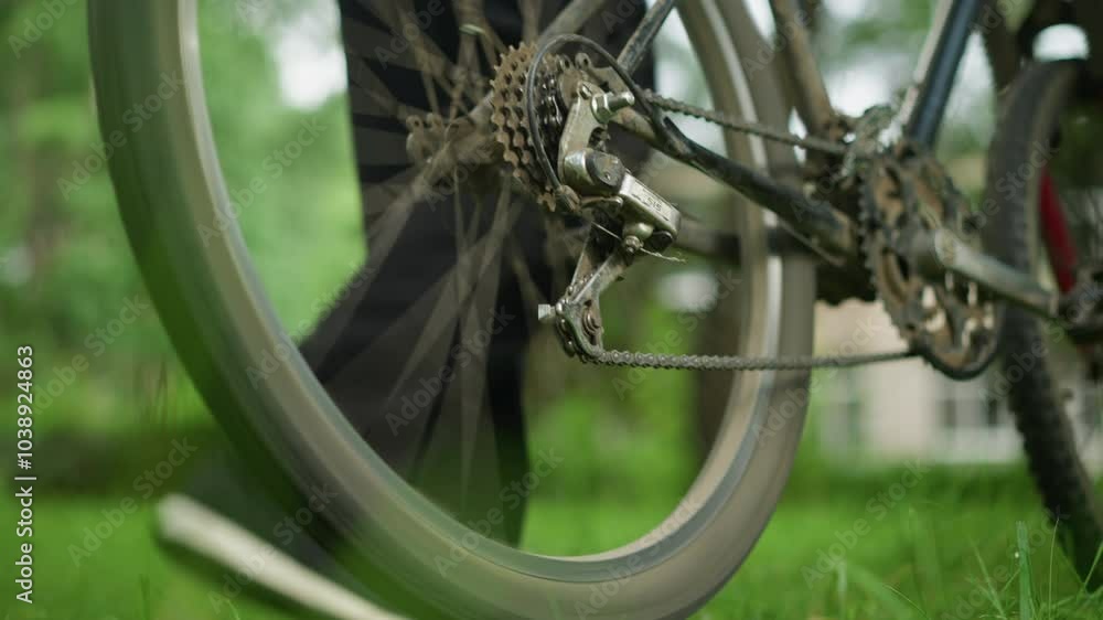 Close-up of individual standing next to a parked bicycle in a grassy field, the person slightly lifts the rear tire and pedals briefly, causing the tire to rotate, with blurred background Close-up of individual standing next to a parked bicycle in a grassy field, the person slightly lifts the rear tire and pedals briefly, causing the tire to rotate, with blurred background