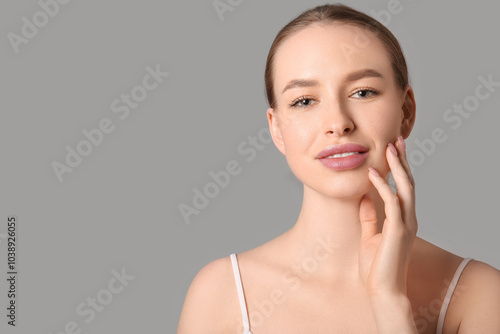 Beautiful young woman touching face on grey background