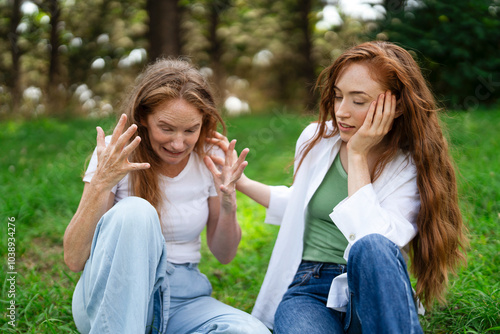 Two women engaged in a heartfelt conversation while sitting on grass in a serene outdoor setting during daytime