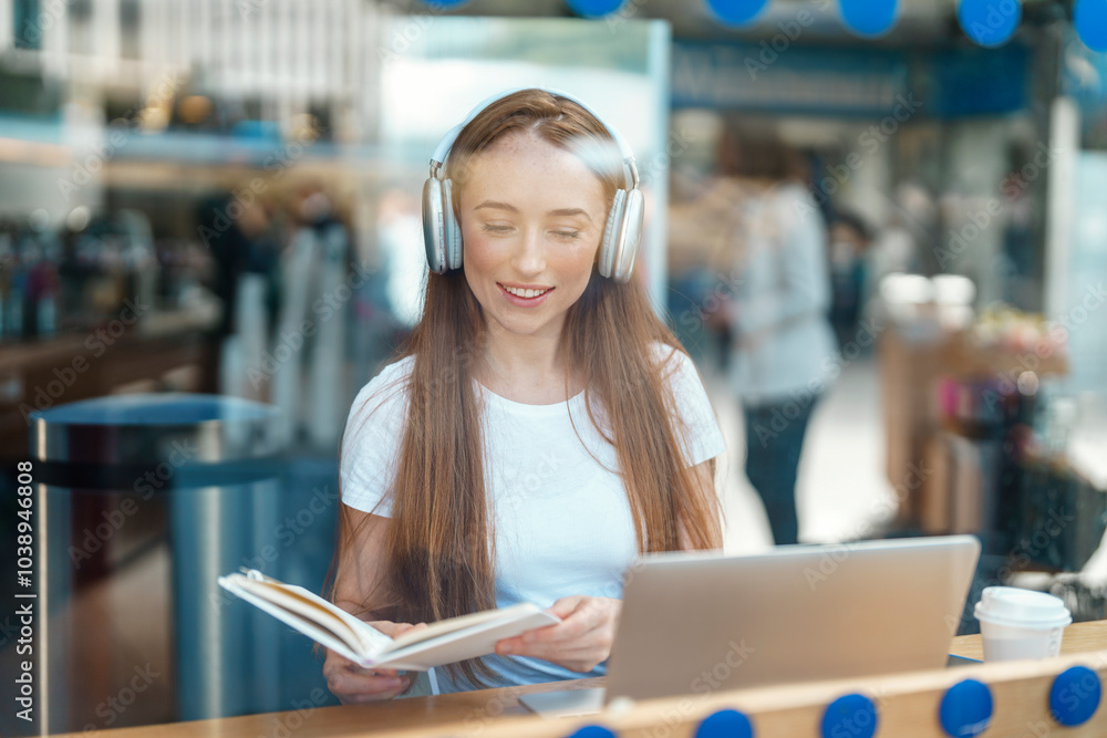 Fototapeta premium Young woman studying diligently in a cozy coffee shop while enjoying soft music, capturing a peaceful afternoon