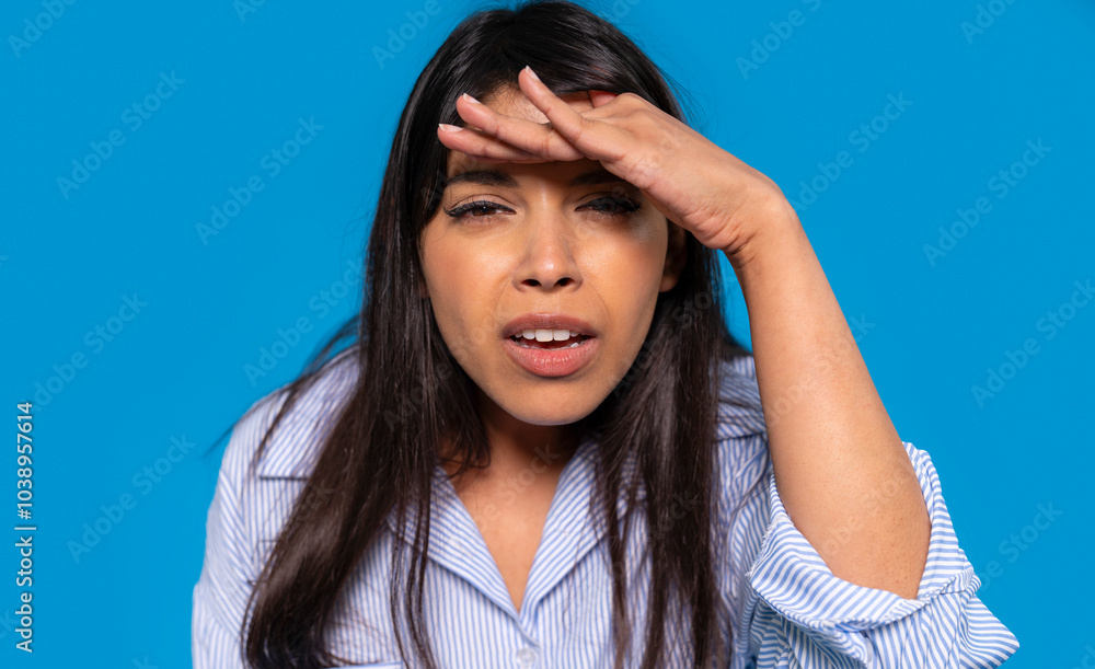 Fototapeta premium A woman shielding her eyes from the bright light while looking out against a vivid blue backdrop