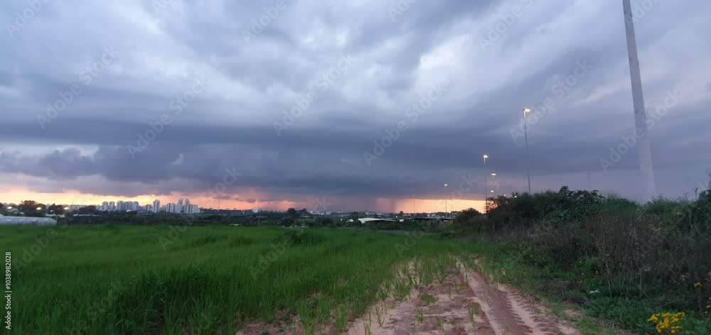 Lightning Stormy clouds and sunset over green fields: thick storm clouds, casting a shadow over a vibrant green field. the setting sun creates a glowing orange horizon behind a city skyline