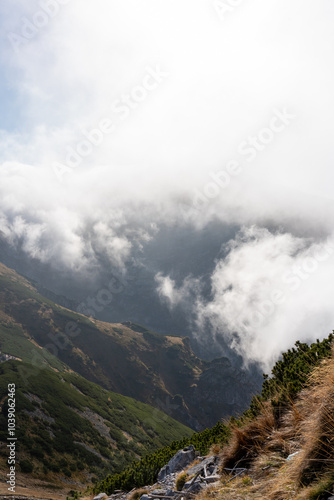 Foggy mountain landscape with sunlight filtering through clouds, revealing rugged cliffs and green slopes. Concept of tranquil nature, dramatic scenery, serene outdoor environment. High quality photo