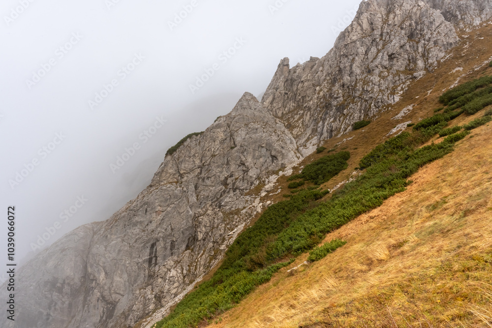 Fototapeta premium Panoramic view of a mountain landscape with rocky slopes and clouds drifting over a valley on a bright day. Concept of nature exploration, outdoor adventure, and peaceful serenity. High quality photo