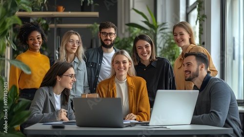 Diverse group of young professionals gathered around a laptop, smiling and engaged in conversation.