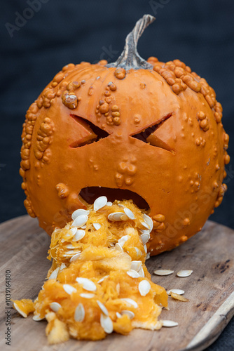 A pumpkin with a face carved into it and a mouth open, spewing out orange pulp. The pumpkin appears to be in a state of distress and throwing up