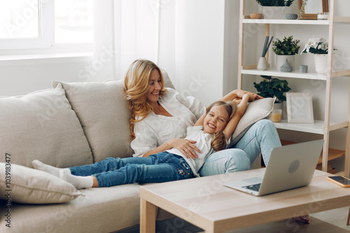 Mother and daughter bonding while watching a video on a laptop, sitting comfortably on a cozy couch together