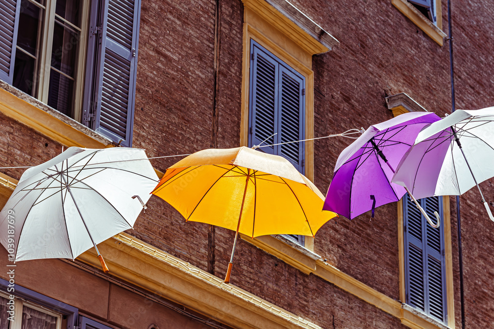 Colorful umbrellas create a vibrant canopy over a charming street in a scenic town of the Modena, Italy,