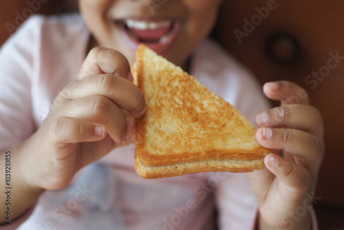 A Joyful Child Happily Holding a TriangleShaped Grilled Cheese Sandwich with excitement photo