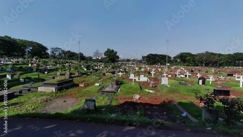 Long continuous take from Motorcycle POV entering the cemetery from a motor vehicle in the morning. Lots of tombstones. Public Burial place under trees on green grass in Jakarta, Indonesia. SSTKPlates photo