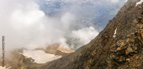 Steep huge rocky way from Tête Rousse Hut with valley, clouds and sun background