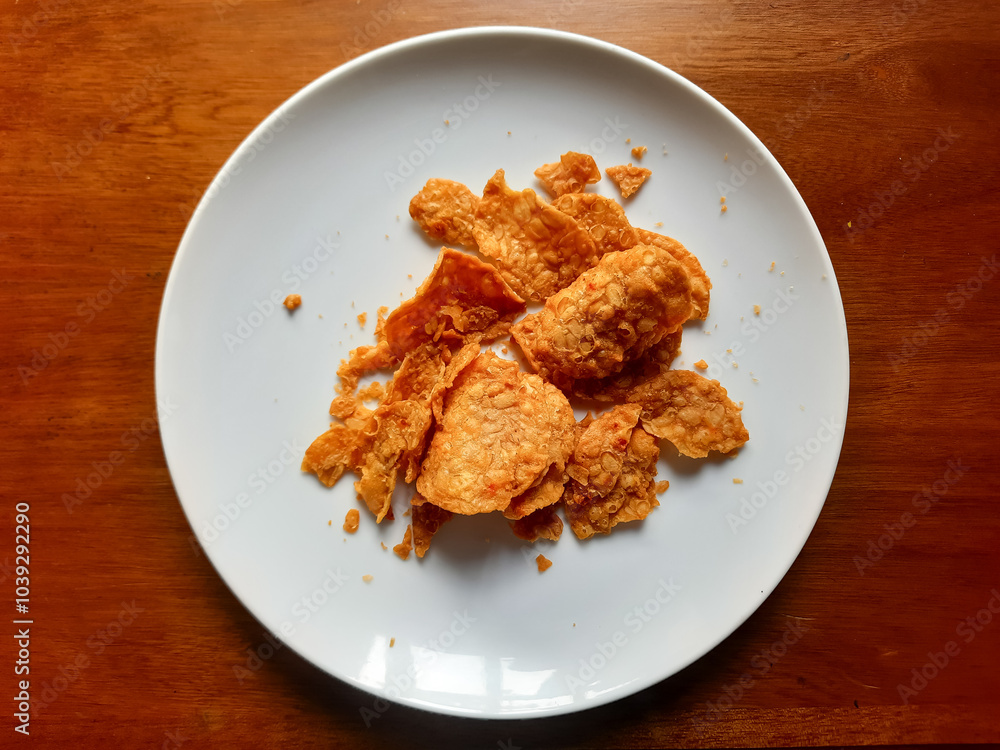 processed from tempeh, namely tempeh chips that are given spicy and salty seasoning on a white plate processed from tempeh, namely tempeh chips that are given spicy and salty seasoning on a white plate