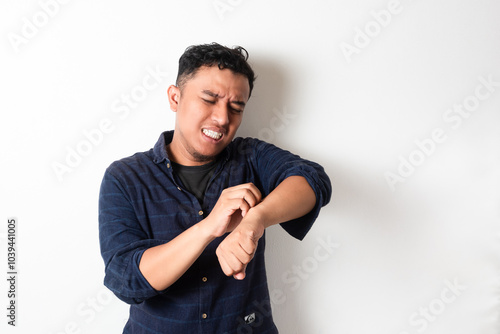 Adult Asian man scratching his hand and showing uncomfortable expression photo