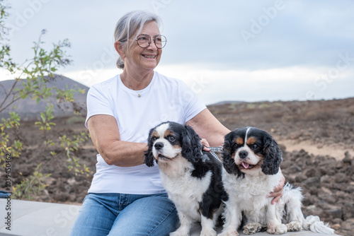 Photography Senior smiling woman sitting outdoors with her two cavalier king charles spaniel dogs enjoying leisure time