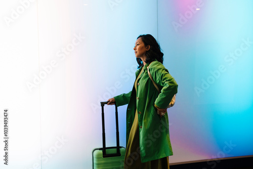 Woman standing with suitcase in front of gradient wall photo