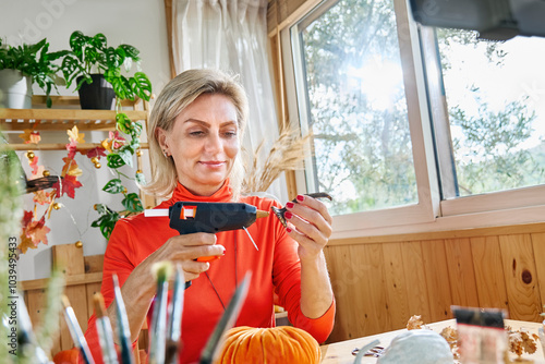 Smiling mature influencer making artificial pumpkin at home photo