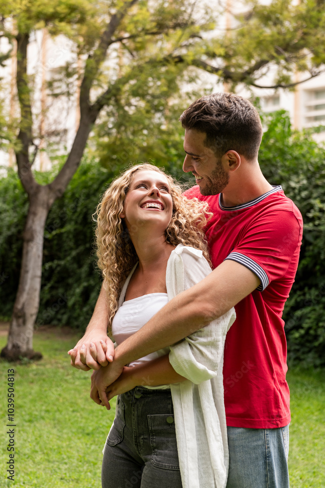 Happy boyfriend embracing girlfriend standing in park Happy boyfriend embracing girlfriend standing in park