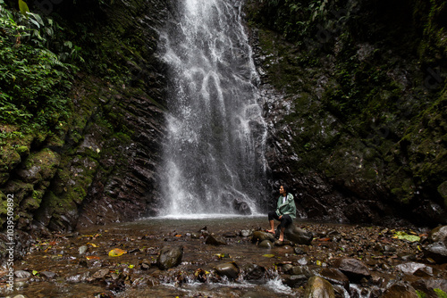 Woman sitting near waterfall in forest photo