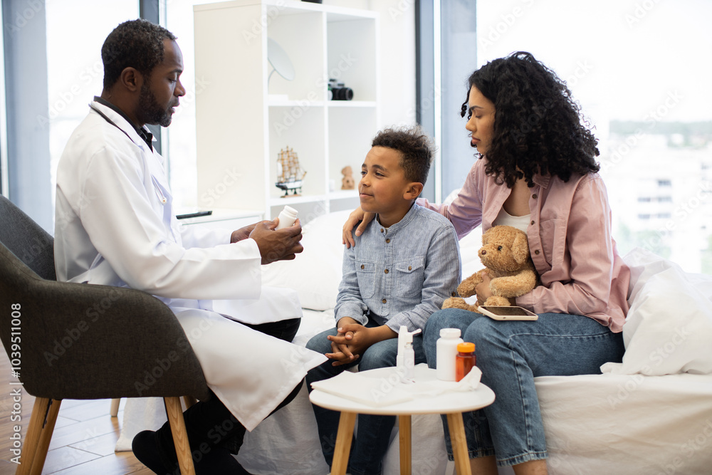 African male doctor examines young boy with concerned African woman comforting him. Doctor offers medicine for recovery at medical check-up. African male doctor examines young boy with concerned African woman comforting him. Doctor offers medicine for recovery at medical check-up.