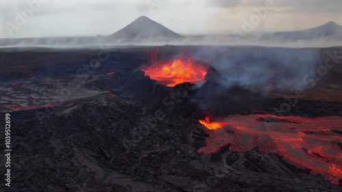 Aerial shot of an active volcanic eruption in Iceland, showcasing glowing lava streams flowing from the crater and thick smoke rising into the sky.