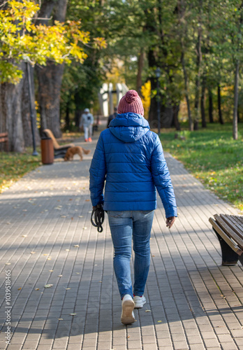 A woman wearing a blue jacket and a red hat walks down a sidewalk