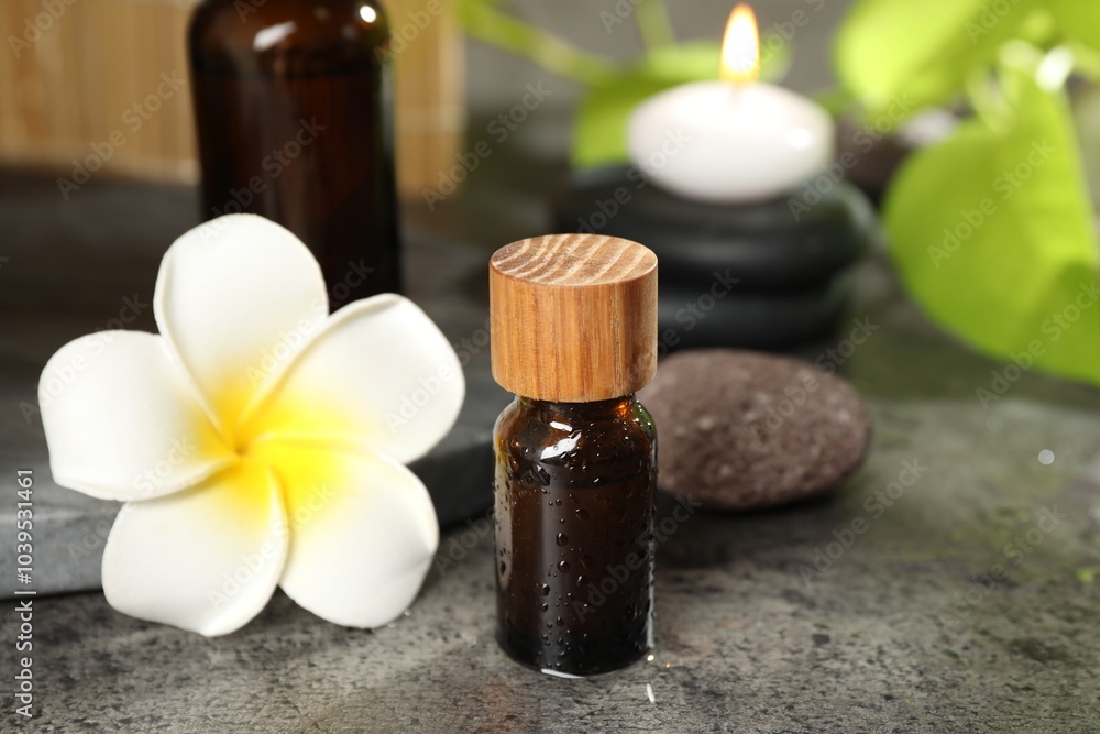 Spa composition with bottles of cosmetic products, plumeria flower and burning candle on grey table, closeup Spa composition with bottles of cosmetic products, plumeria flower and burning candle on grey table, closeup