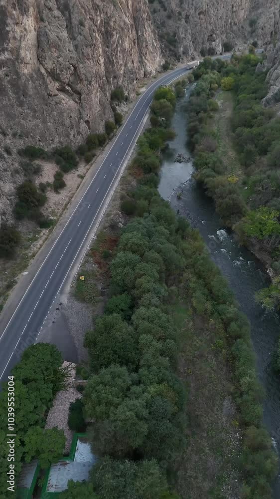 Vertical drone shot along a scenic road between rocky hills and green trees Vertical drone shot along a scenic road between rocky hills and green trees