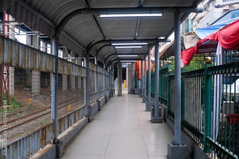 Obraz premium A covered pedestrian walkway near a train station in Jakarta, Indonesia, features metal fencing and a tiled floor. 