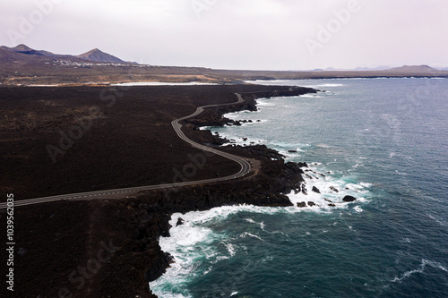 drone view of foamy sea breaking over the volcanic coast with curved roadway at Los Hervideros in Yaiza, Lanzarote at Canary Islands, Spain, concept of wild nature photo