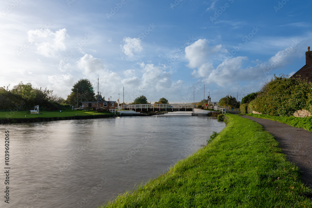A swing bridge on a canal with a green bank and blue sky with clouds A swing bridge on a canal with a green bank and blue sky with clouds