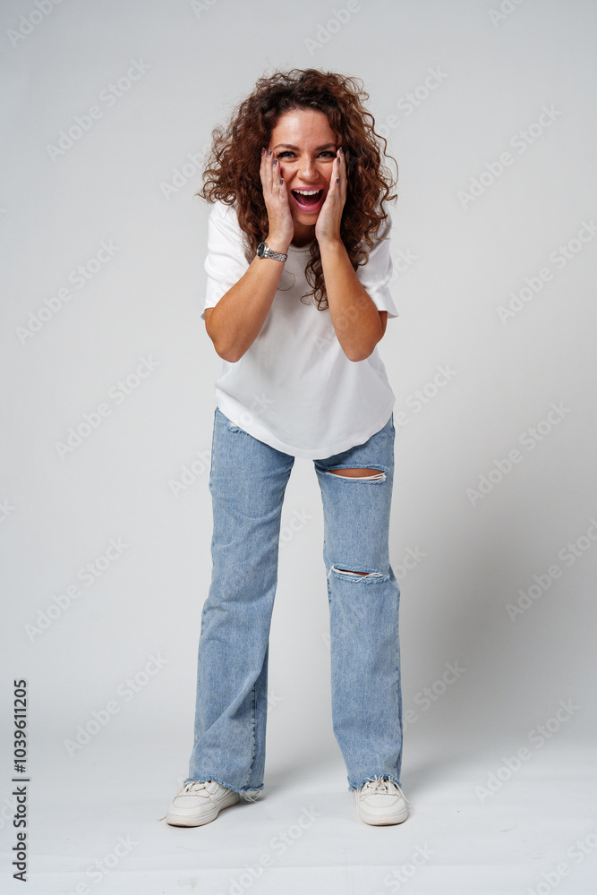 A woman in a white shirt and ripped jeans posing positively with a playful expression in a light studio setting A woman in a white shirt and ripped jeans posing positively with a playful expression in a light studio setting