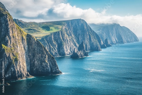 Majestic cliffs line the coast, towering above the tranquil sea. Lush greenery covers the top as dramatic rock formations plunge into azure waters below.