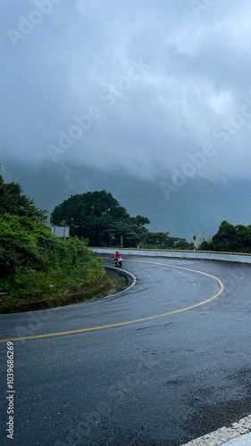 Bild auf Leinwand A motorcyclist navigates a winding mountain road on a misty day, symbolizing adv