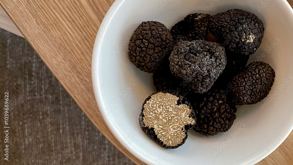 A bowl of fresh black truffles on a wooden table symbolizes gourmet cuisine and luxury in European culinary traditions A bowl of fresh black truffles on a wooden table symbolizes gourmet cuisine and luxury in European culinary traditions