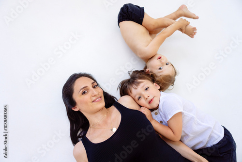 Φωτογραφία A young pregnant woman with her cute sons in casual clothes are lying on a white floor