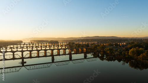 Aerial view of multiple bridges crossing the Susquehanna River at sunrise in Harrisburg, Pennsylvania, with the city skyline and surrounding landscapes bathed in golden light. photo