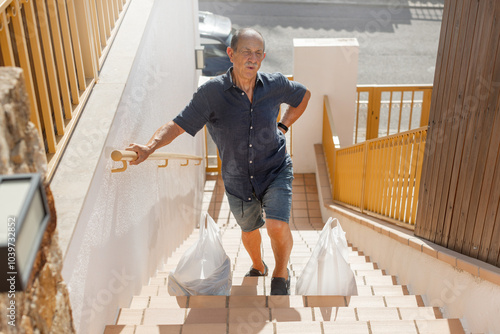 Fotografi Elderly caucasian man holds his back with painful face because carrying heavy groceries, painful expression, twisted face