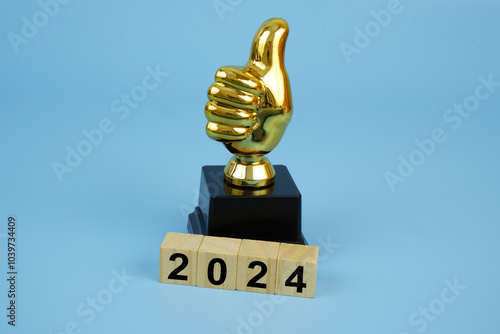 Gold champion thumbs up trophy cup and cubes with numbers 2024 on blue background. Best things in year 2024 concept. photo