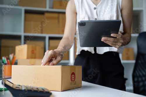 Entrepreneur Managing Small Business Operations with Tablet in Modern Office Setting Surrounded by Shipping Boxes and Supplies