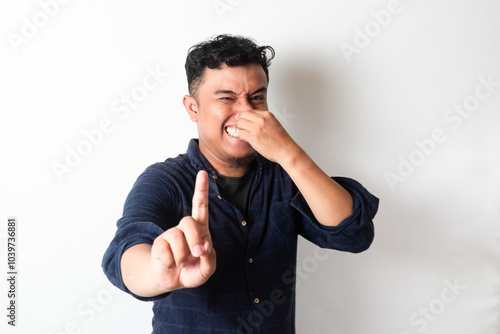 Adult Asian man covering nose with smelly expression by showing 1 finger