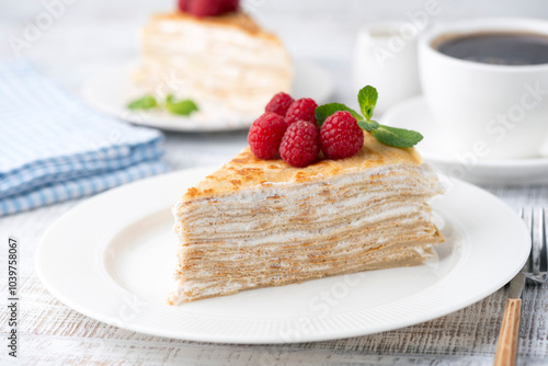 Crepe cake with custard cream served with fresh raspberries on a white plate, closeup view