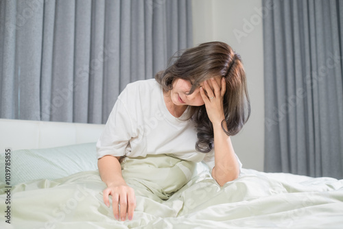 A woman lying in bed with her hand resting on her forehead, visibly uncomfortable due to a headache while checking for a fever. The soft bedding contrasts with the signs of unease, portraying a moment
