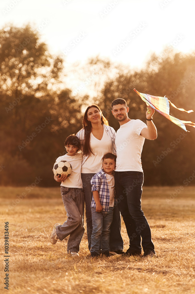 Fototapeta premium Vacation time. Family of father, mother, daughter and son that are standing in the field, with kite in hand