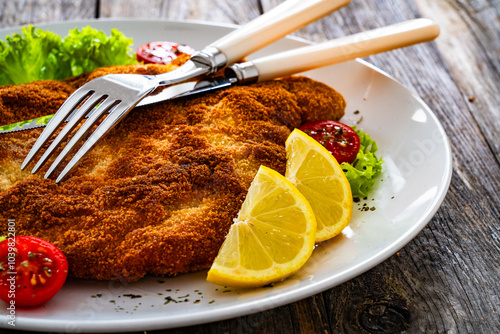 Crispy breaded fried pork chop and fresh vegetables on wooden table
